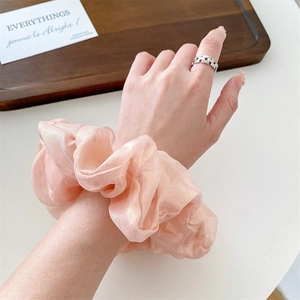 Pink mermaid fabric scrunchie with glossy finish worn on wrist over a white desk