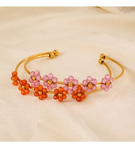 Detail of gold open bangles with pink and orange beaded flower charms on beige fabric