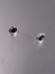 Macro shot of 925 sterling silver stud earrings with oval black gemstones on grey surface