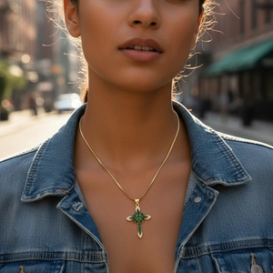 Detailed view of 18K gold cross necklace with green zircon stones on a denim jacket