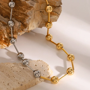 Minimalist 18k gold and silver stainless steel ball necklace on natural rock surface