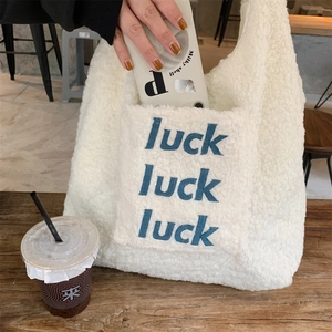 Detail der weißen Plüsch-Tragetasche mit Luck-Stickerei in einem gemütlichen Café