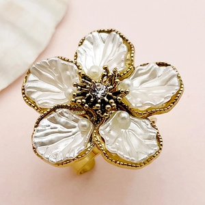 Macro detail of gold flower ring with white shell petals and central zircon stones