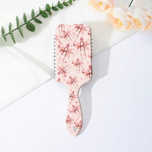 Close-up of pink hair brush with bow and lipstick patterns on a minimalist floral setup