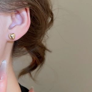 Close-up of minimalist heart-shaped gold stud earring worn by a model in warm light