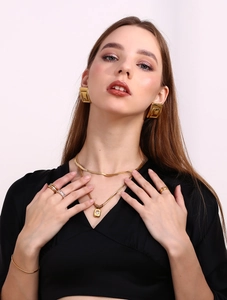 Detailed view of women wearing gold rectangular earrings and layered snake bone necklaces