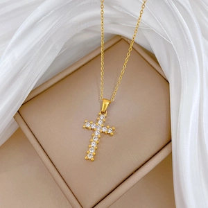 Close-up of gold titanium cross pendant with clear cubic zirconia on white silk
