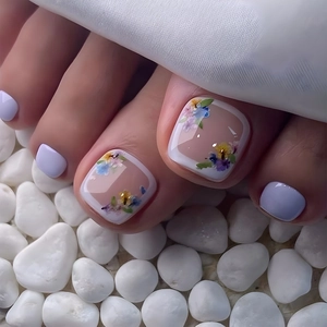 Detail of French style purple and white flower pattern toenail tips on white pebbles