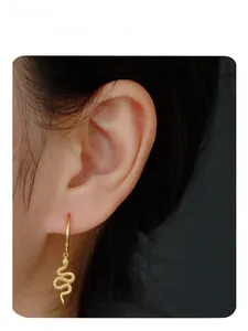 Close-up of model wearing gold snake-shaped dangle earrings with textured detail