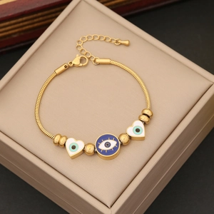 Gold snake chain bracelet featuring blue evil eye and white heart charms in a jewelry box