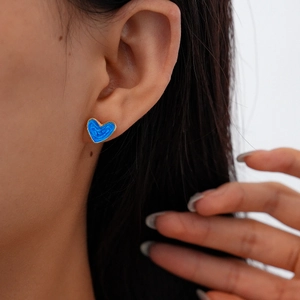Close-up of heart-shaped gold stud earring with blue enamel swirl on model's ear