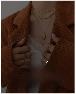 Detail of layered gold necklaces with vintage pendants and emerald rings on a blazer