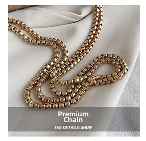 Close-up of premium polished gold box chain strap on soft beige pleated fabric