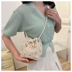 Detailed view of cream woven bucket bag featuring green floral embroidery and drawstring