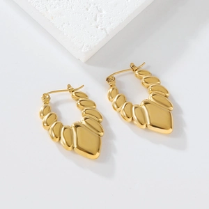 Macro shot of gold textured earrings with a modern sculptural design on a stone background