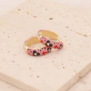 Close-up of golden hoop earrings featuring colorful enamel floral patterns on stone tray