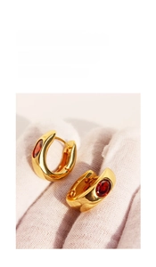 Close-up of golden U-shaped hoop earrings with oval-cut red ruby gemstones