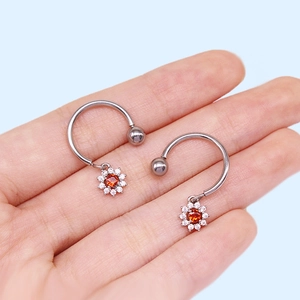 Close-up of a silver U-shaped sunflower nipple ring featuring an orange gem and crystals