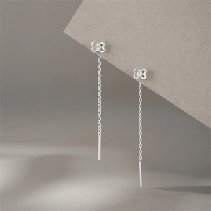 Macro shot of silver heart-shaped earring with dangling long tassels on grey steps