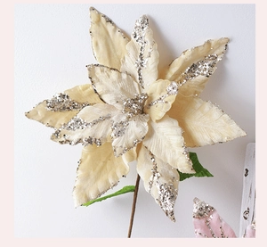 Detailed view of artificial cream poinsettia flower with silver glitter and green leaves