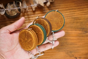 Close-up of four handmade leather measuring tapes in assorted colors on wood