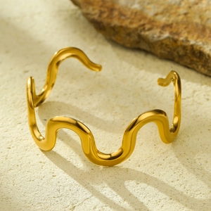 Detail shot of golden wave-shaped 18K gold plated stainless steel open bangle bracelet