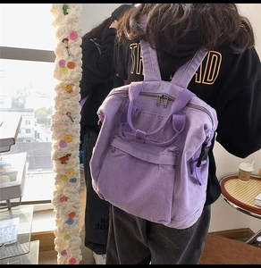 Close-up of a purple canvas backpack with front zipper pocket and silver metal hardware
