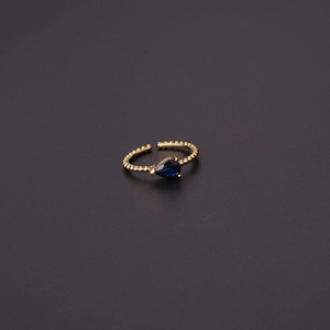 Macro detail of adjustable gold-plated ball-textured ring with a blue teardrop zircon