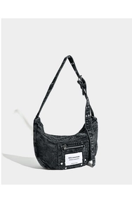 Macro shot of black washed denim crescent bag with metallic eyelets and zipper pocket