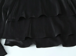 Close-up of black satin shirt featuring layered ruffle design and silky lustrous texture