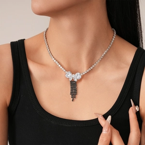 Close-up of a silver bow necklace with black tassels and zircon stones on a female model