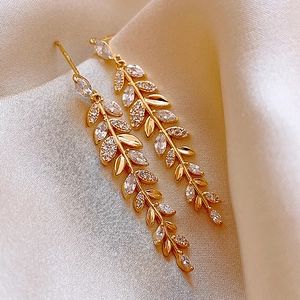 Gros plan de boucles d'oreilles feuilles dorées avec zircon sur fond de soie