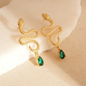 Detail of gold snake earrings with green teardrop gems on a white stone background