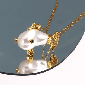Macro shot of gold fish pendant with pearl body and blue gem eye on a reflective mirror