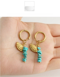Close-up of golden fan-shaped earrings with blue turquoise stones on palm