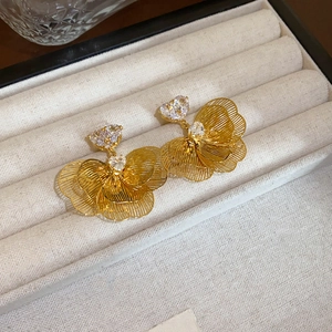 Close-up of golden hollow flower earrings with heart-shaped crystal centers on velvet