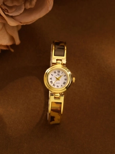 Detail of vintage gold and tortoiseshell chain watch with a white Roman numeral dial