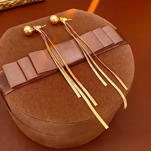 Goldene Schlangenketten-Ohrhänger auf brauner Geschenkbox mit elegantem Licht und Schatten