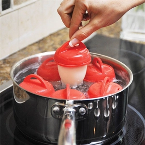 Detail of six red silicone egg cooker cups boiling in a pot with one lifted by hand