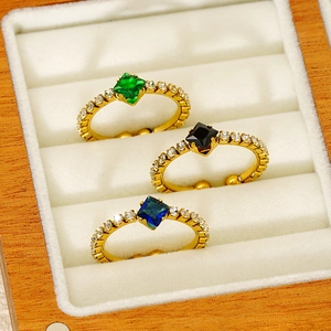 Three gold adjustable rings with green, black, and blue square stones in a wooden jewelry box