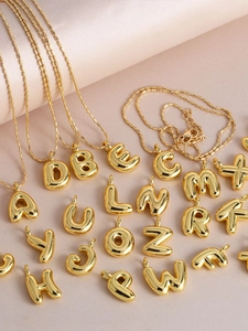 Detail of 26 golden bubble letters pendants on pink satin fabric with dainty bead chains