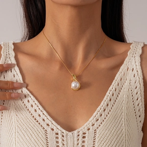 Close-up of a gold necklace featuring a round faux pearl pendant and zircon knot detail