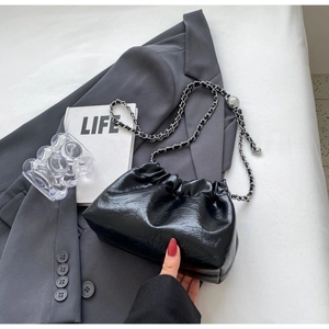 Detail of black pleated cloud bag with silver chain strap on a dark blazer