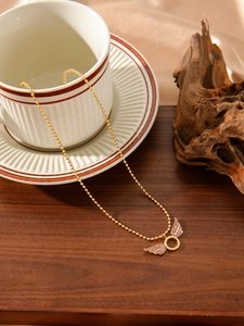 Detailed shot of a gold beaded necklace with a pink crystal-studded angel wing pendant