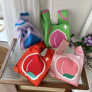 Close-up of four colorful knitted mini tote bags with peach patterns on glass table