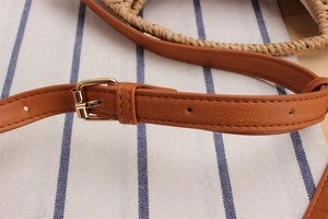 Close-up of brown leather strap with adjustable gold buckle on a woven paper bag