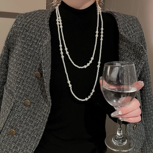 Detail of layered white pearl necklace worn over black turtleneck and tweed jacket