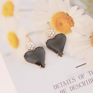Macro shot of asymmetric heart earrings with black stones and gold flower accents
