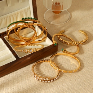 Detailed close-up of gold stainless steel cable bracelets with emerald and zircon inlays