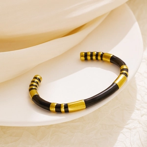 Macro shot of segmented black and gold open bangle on white silk background